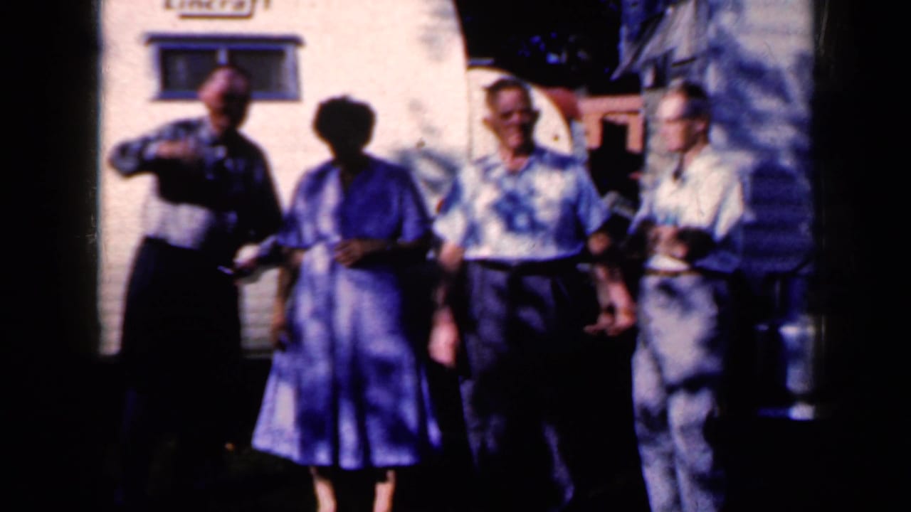 Four older adults stand outside a white trailer, one man saluting toward the camera.
