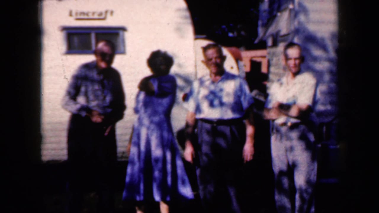 The group remains outside the white trailer in Iowa, with the woman in a blue dress turned toward the men.