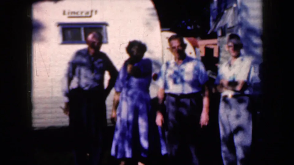 A soft 8mm frame shows older adults standing close together outside a white trailer in a 1959 Iowa home movie.
