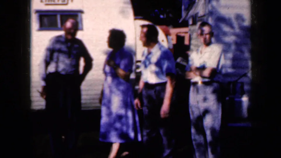 The group stands beside the trailer at the end of the brief 1959 Iowa home-movie shot, with faces partly softened by shadow.