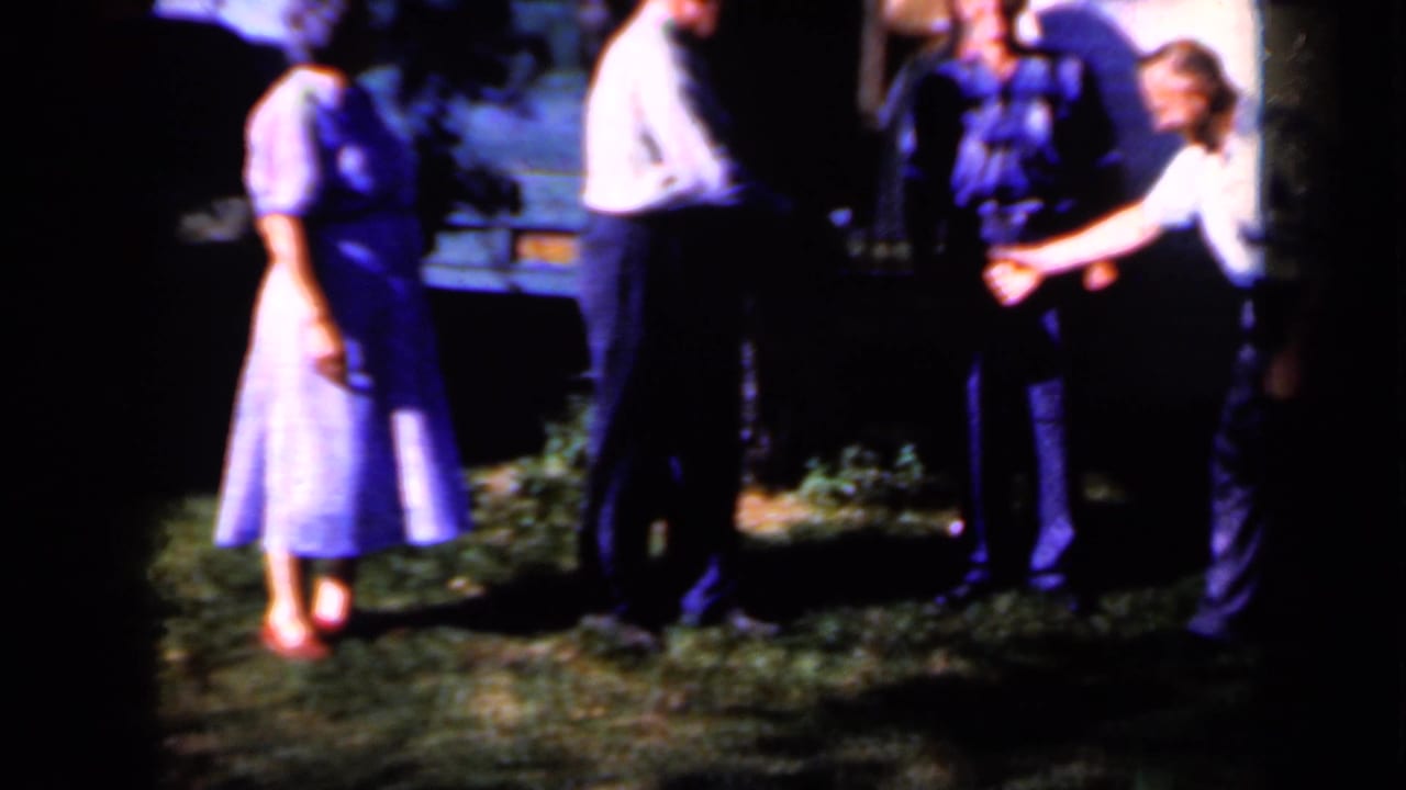 Adults stand on grass near a lit wall as two men appear to shake hands.