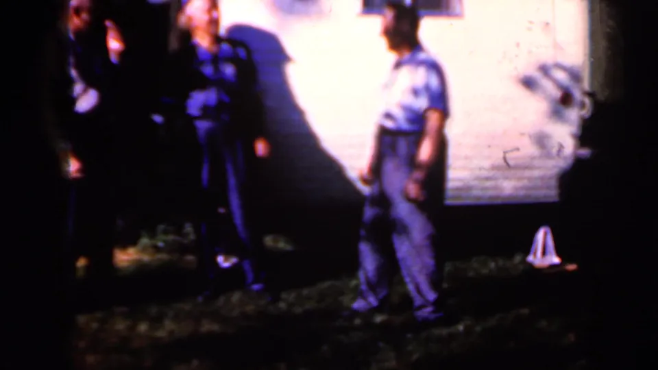 1959 Iowa 8mm frame with a man in a short-sleeve shirt moving near other adults and a lit wall at night.