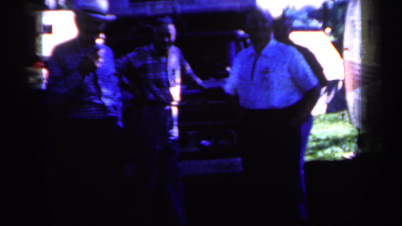 Three men in hats stand in a dark outdoor area near a vehicle.