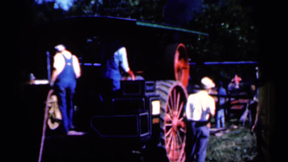 At the end of the 1959 Iowa clip, a man in a light shirt stands near a large red wheel as others remain beside the farm machine.