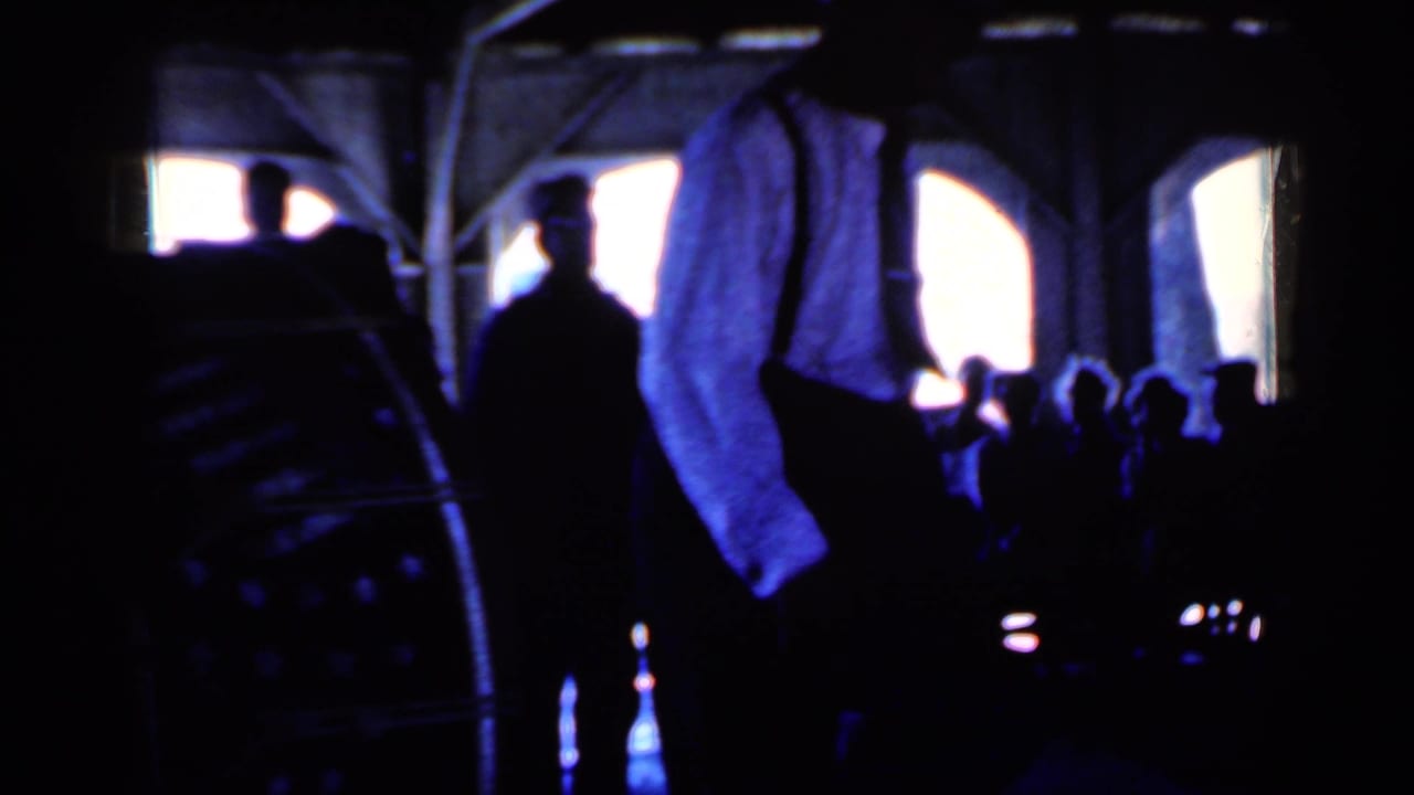 Silhouetted guests in a dark interior, with a man in a light shirt near bright arched openings.