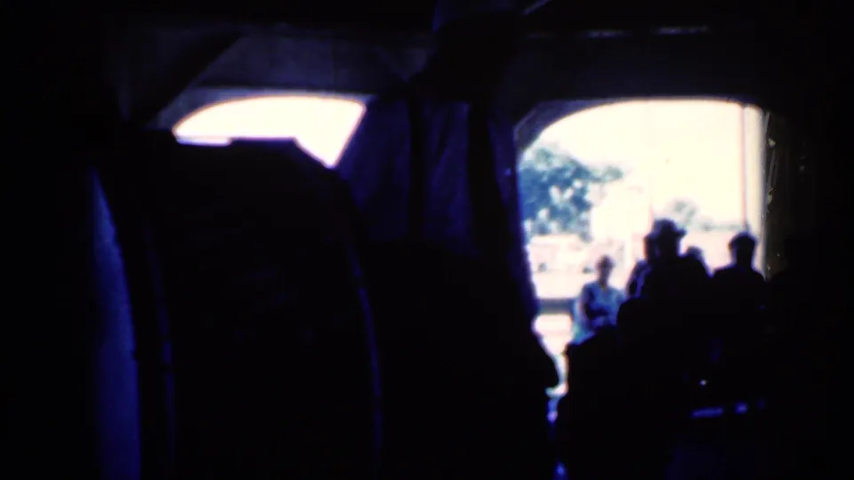 1959 Iowa party frame looking past dark silhouettes toward an overexposed arched opening and people near the light.