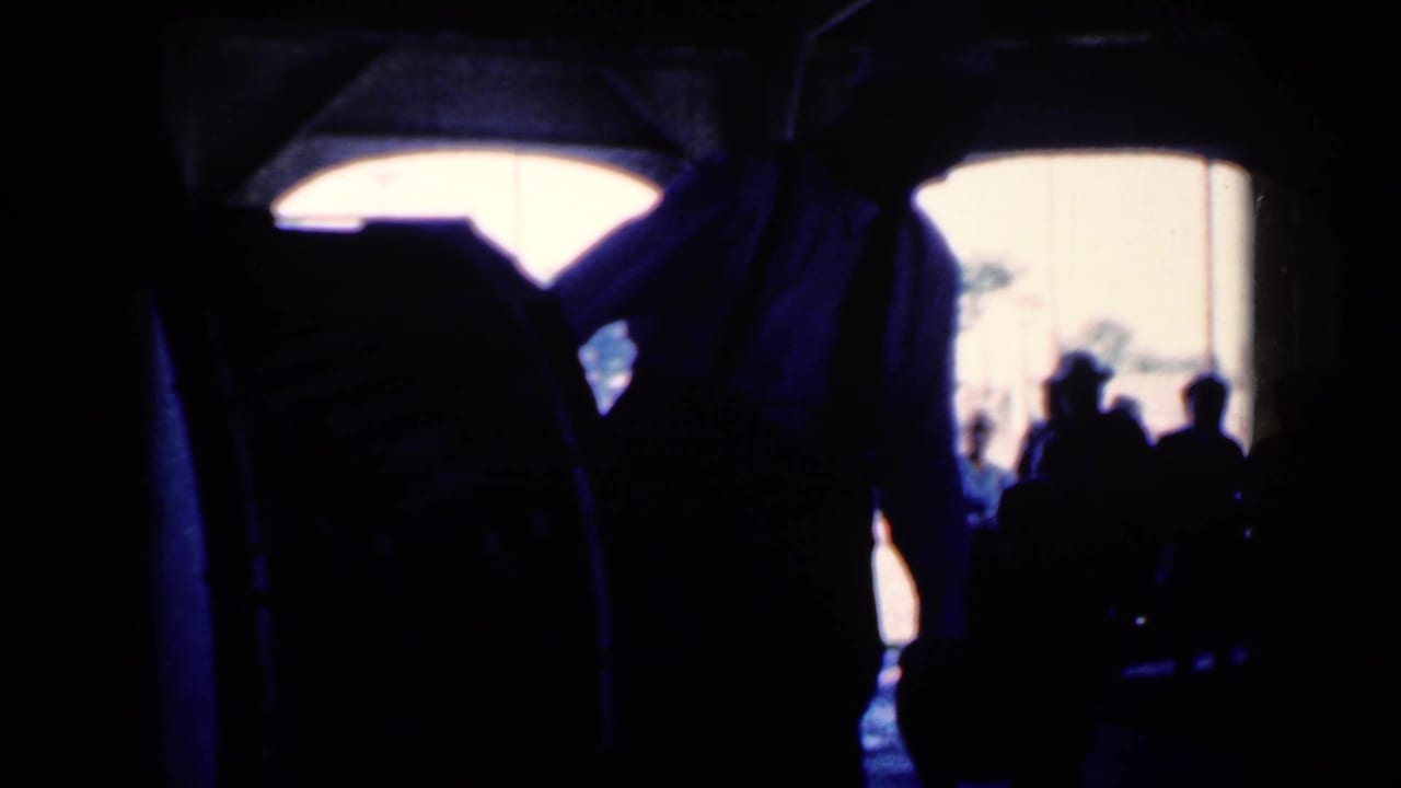 Dark hall interior with silhouetted people watching a white-shirted performer near bright arched openings.