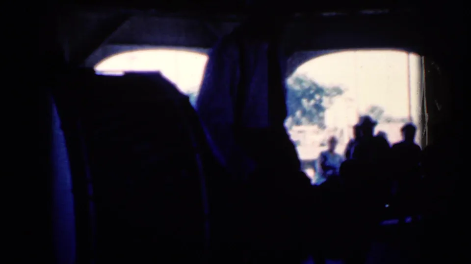 Dim 1959 Iowa home-movie frame with shadowed onlookers, a bright arched opening, and the performer partly obscured by darkness.
