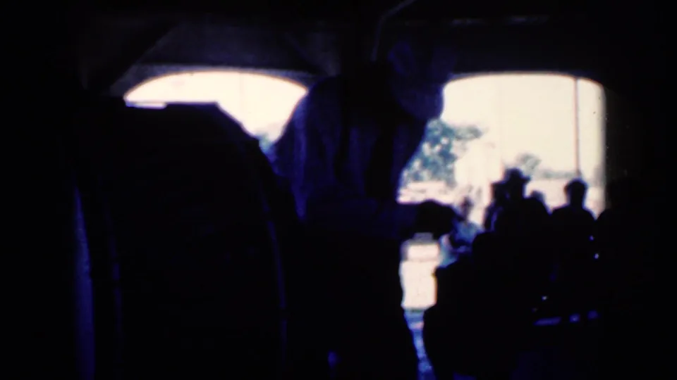 1959 Iowa 8mm frame showing the white-shirted dancer near a small audience in a dark hall, with bright daylight through arched openings.