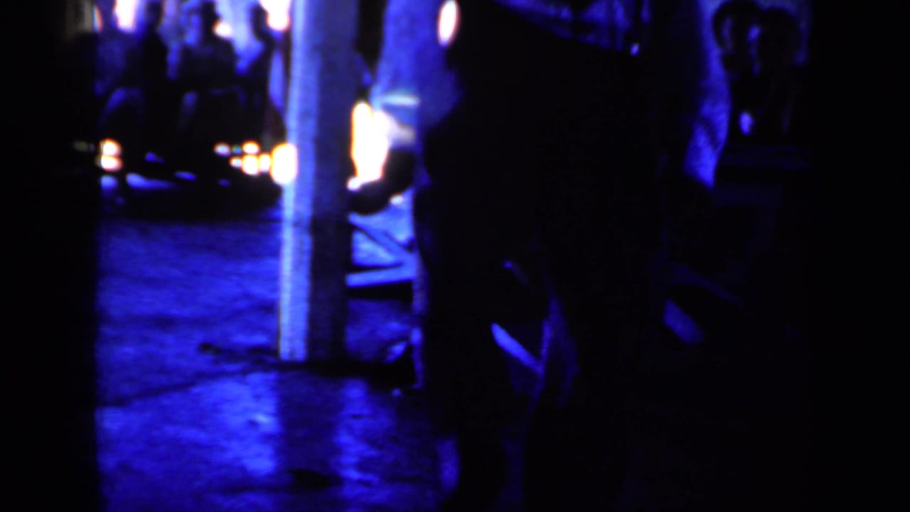 Dark blue train platform with silhouetted people and bright lights in the background.