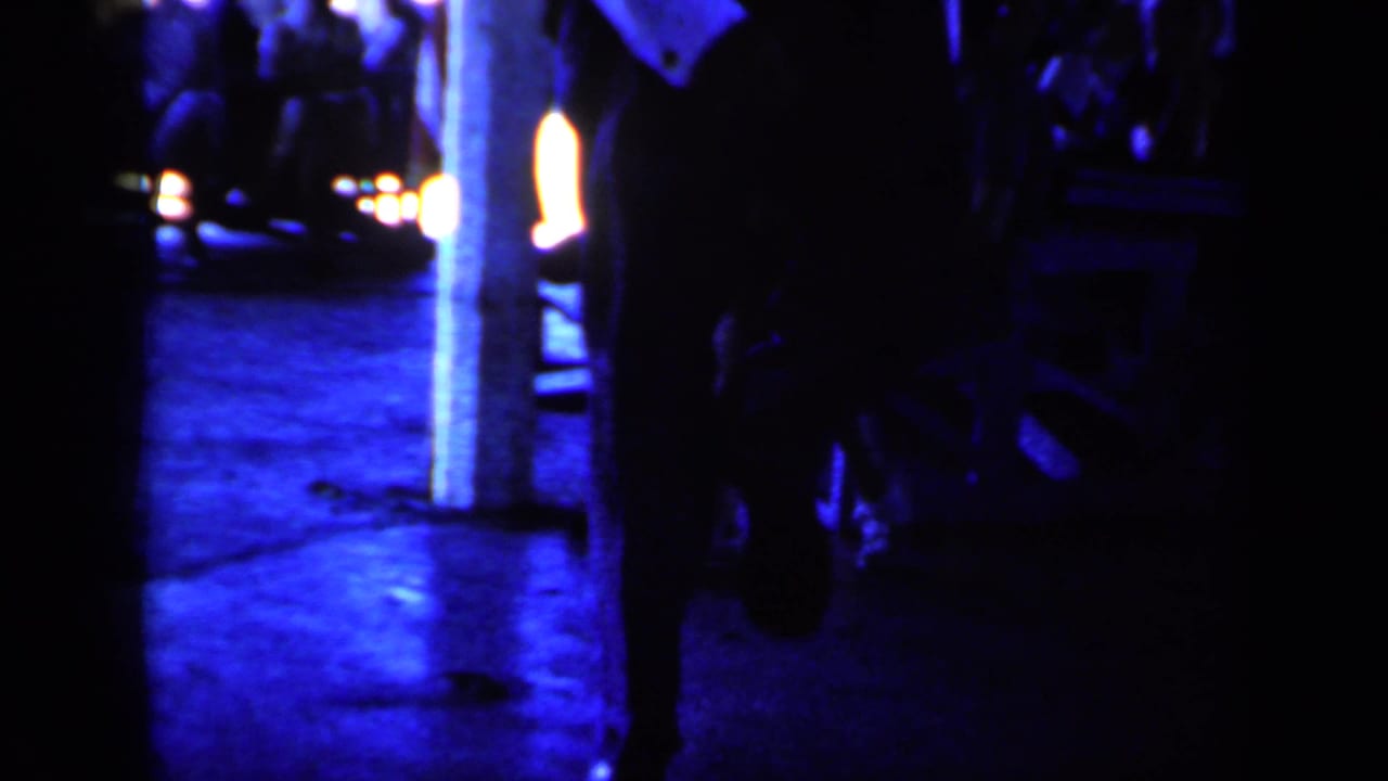 Dim platform scene with dark figures, bright lights, and reflective ground.