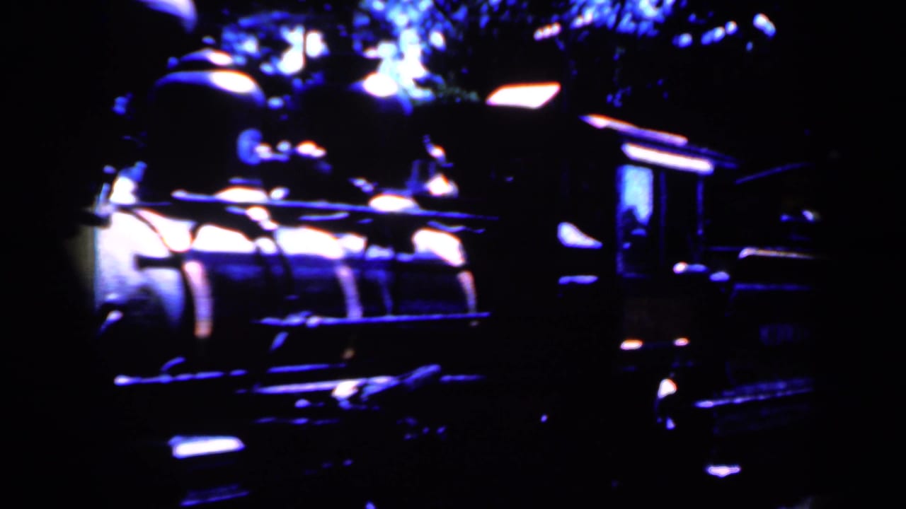 Dark locomotive seen close up with bright reflections and trees behind it.