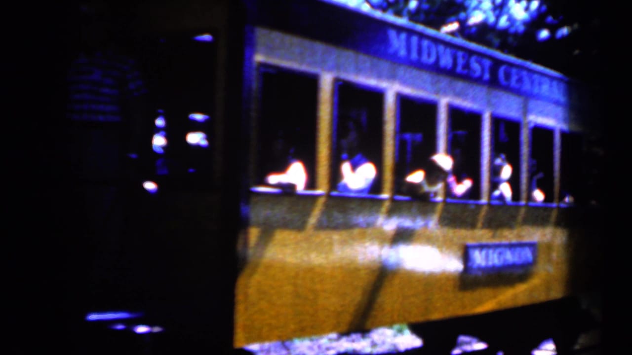 1959 Iowa 8mm frame of a yellow Midwest Central R.R. trolley car moving past in low light, with passengers seen inside.