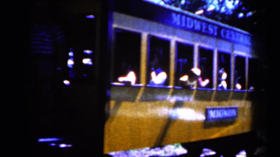 1959 Iowa 8mm frame of a yellow Midwest Central R.R. trolley car moving past in low light, with passengers seen inside.