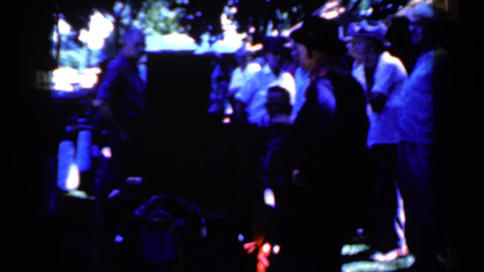 1959 Iowa 8mm frame of spectators gathered in blue-tinted night light near a dark structure after the trolley passes.