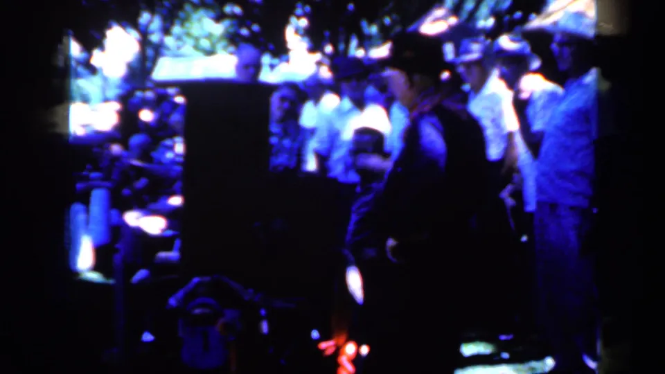 1959 Iowa home-movie frame of people watching near the trolley area, with strong blue shadows and bright light flares.
