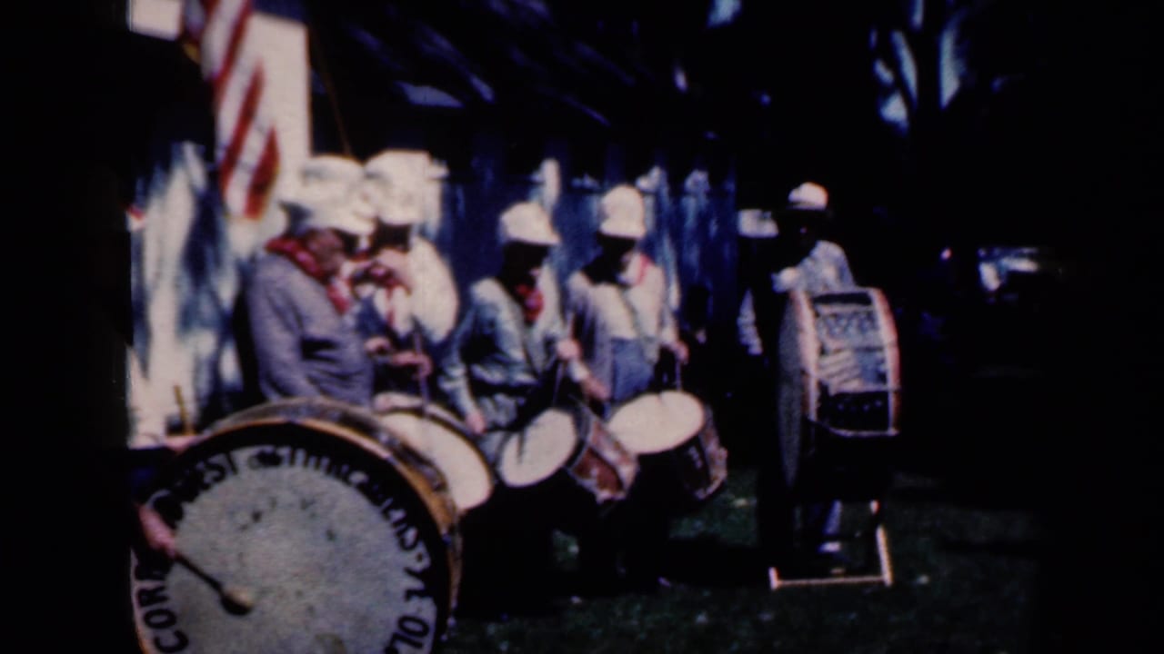 Uniformed drummers play outdoors near a bass drum and U.S. flag.