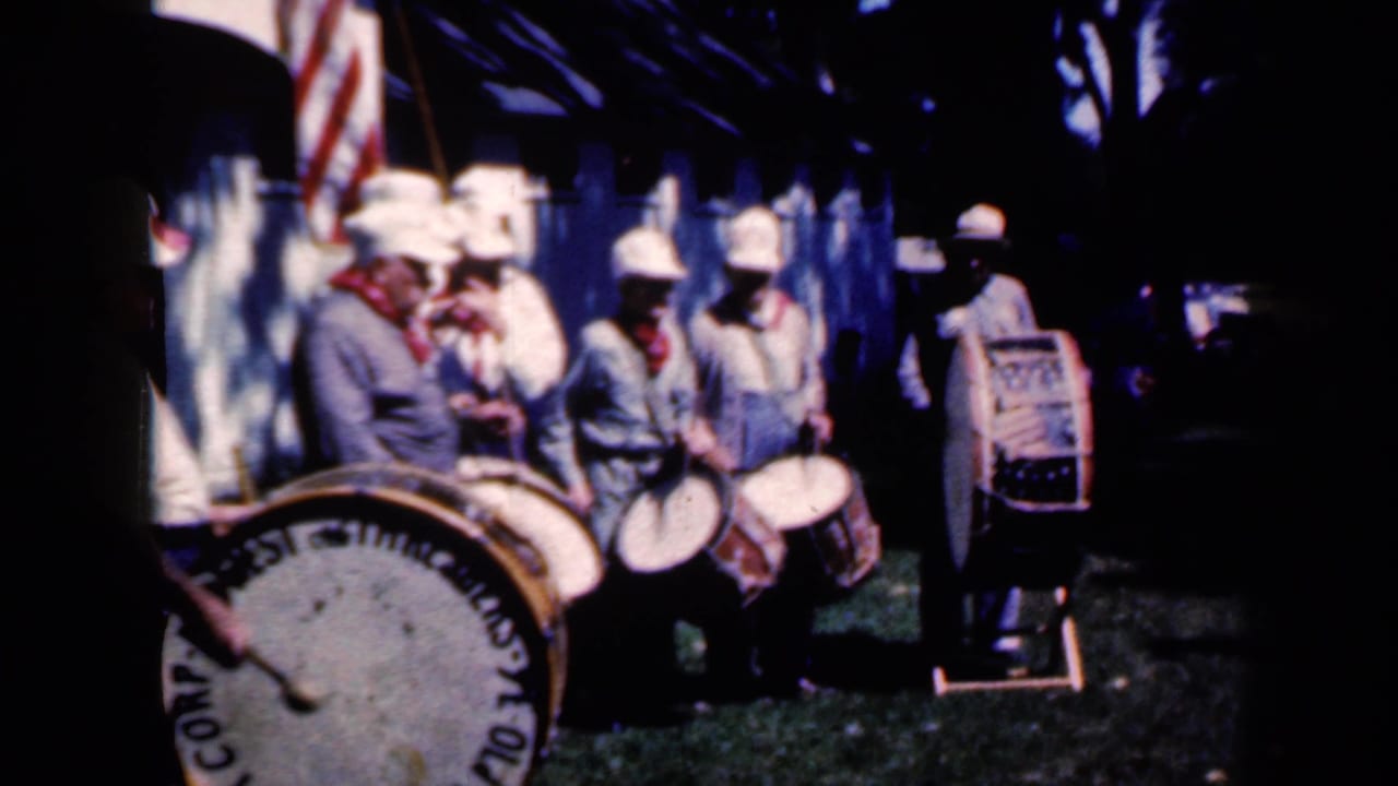 1959 Iowa frame with a small drum group in light uniforms, a prominent bass drum, and an American flag partly visible behind them.
