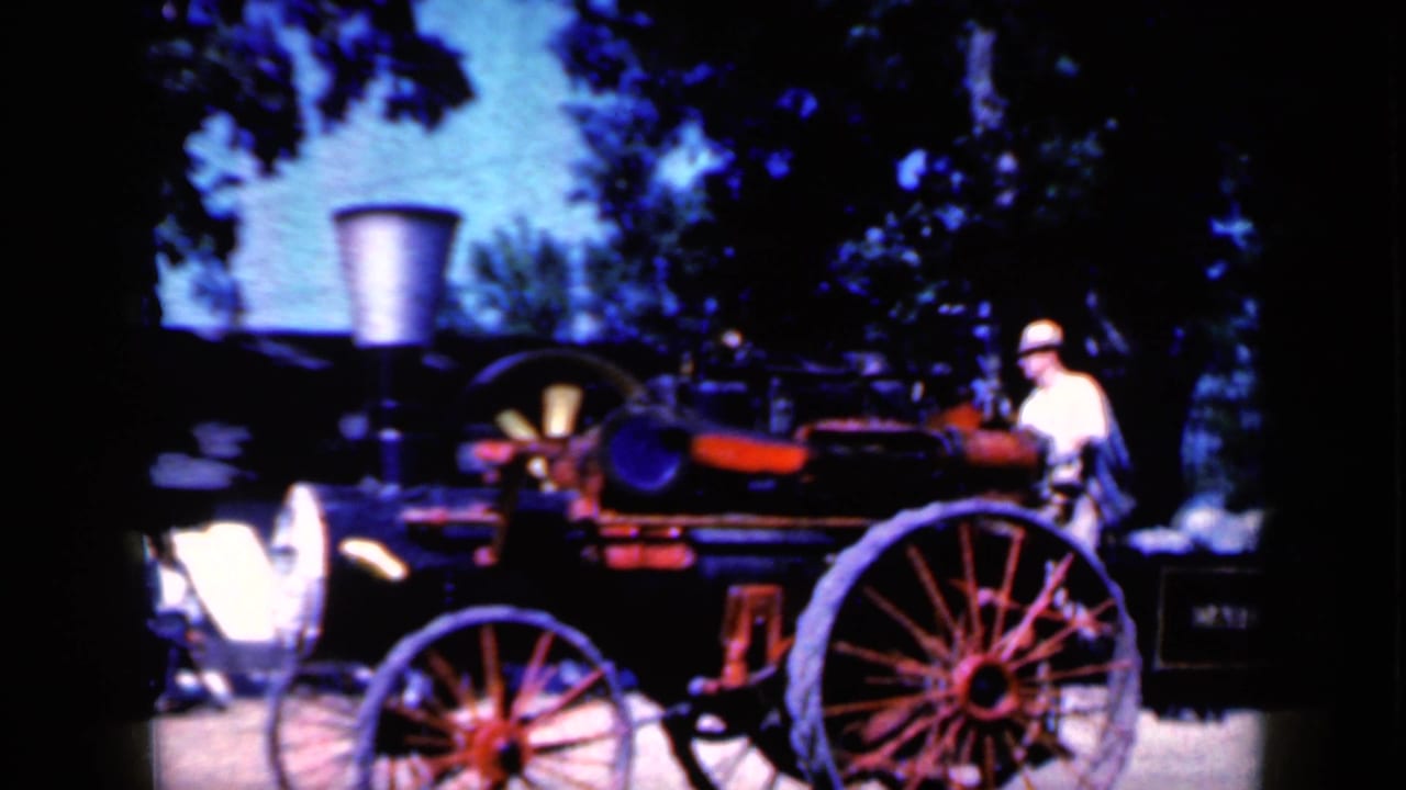 Steam tractor with large spoked wheels beside an adult in a hat at an outdoor event.