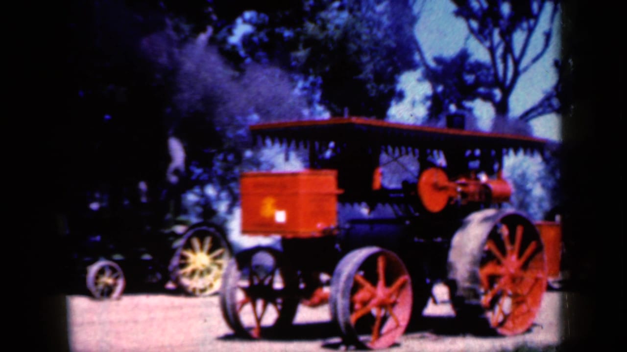 Red and black steam tractor shown in profile with steam rising near trees.