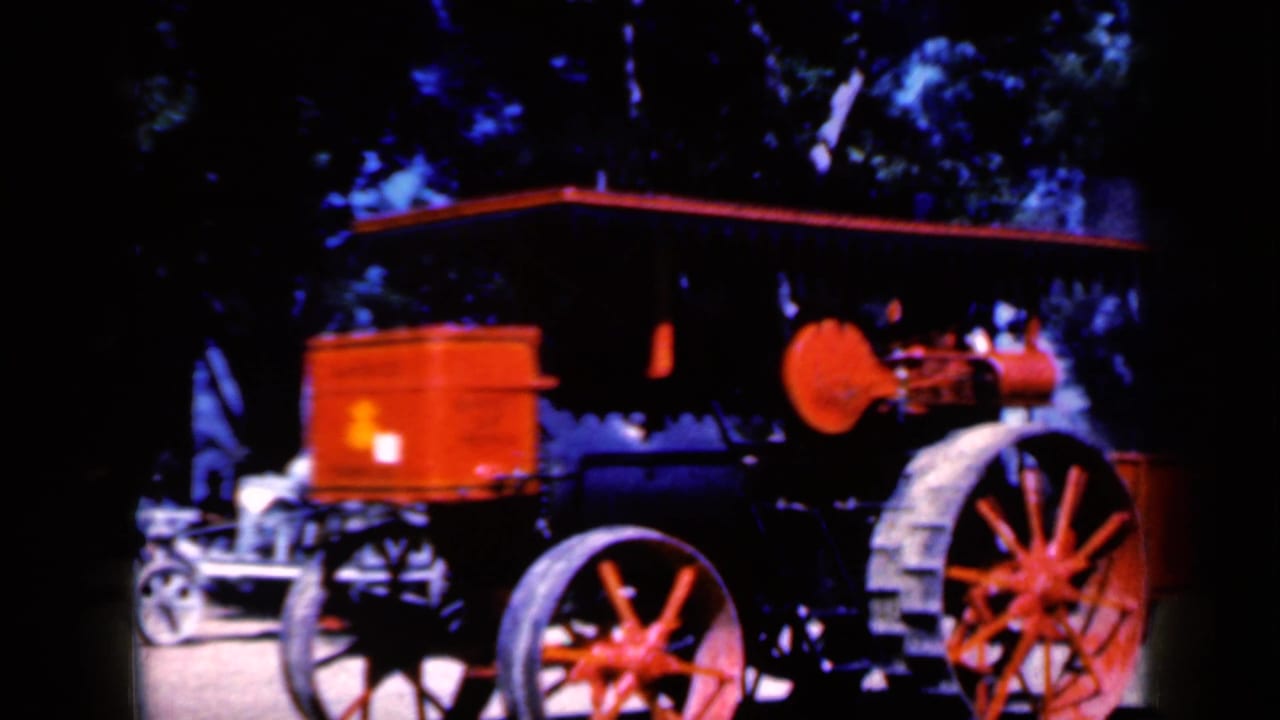 Red and black steam-powered vehicle with large red wheels under trees.
