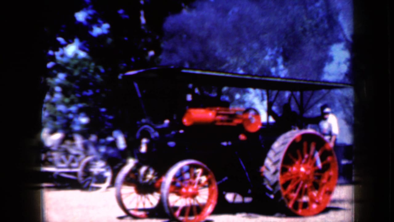 The steam-powered vehicle appears in profile with red wheels, a dark canopy, smoke or steam, and an adult standing nearby.