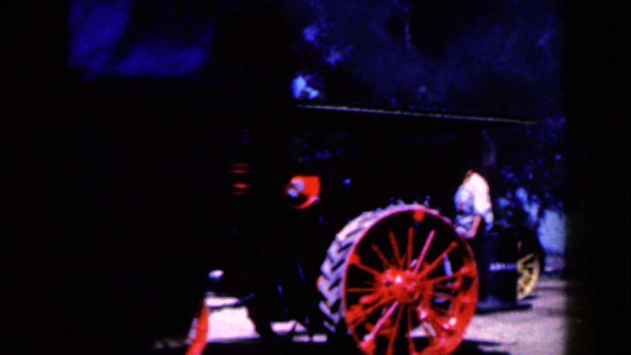 Red-wheeled steam tractor partly framed at an outdoor display with a man standing nearby.