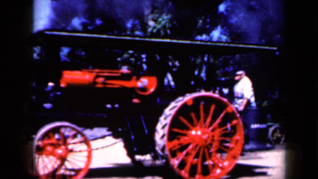 A vintage steam tractor in Iowa, 1959, appears in side view with a red boiler, large red wheel, and a man standing near the rear.