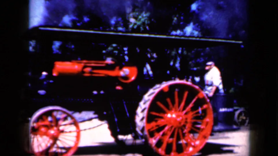 A vintage steam tractor in Iowa, 1959, appears in side view with a red boiler, large red wheel, and a man standing near the rear.