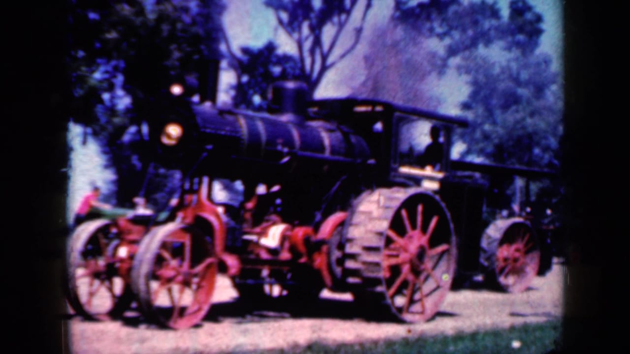 Black steam tractor with red wheels on a dirt path among trees.