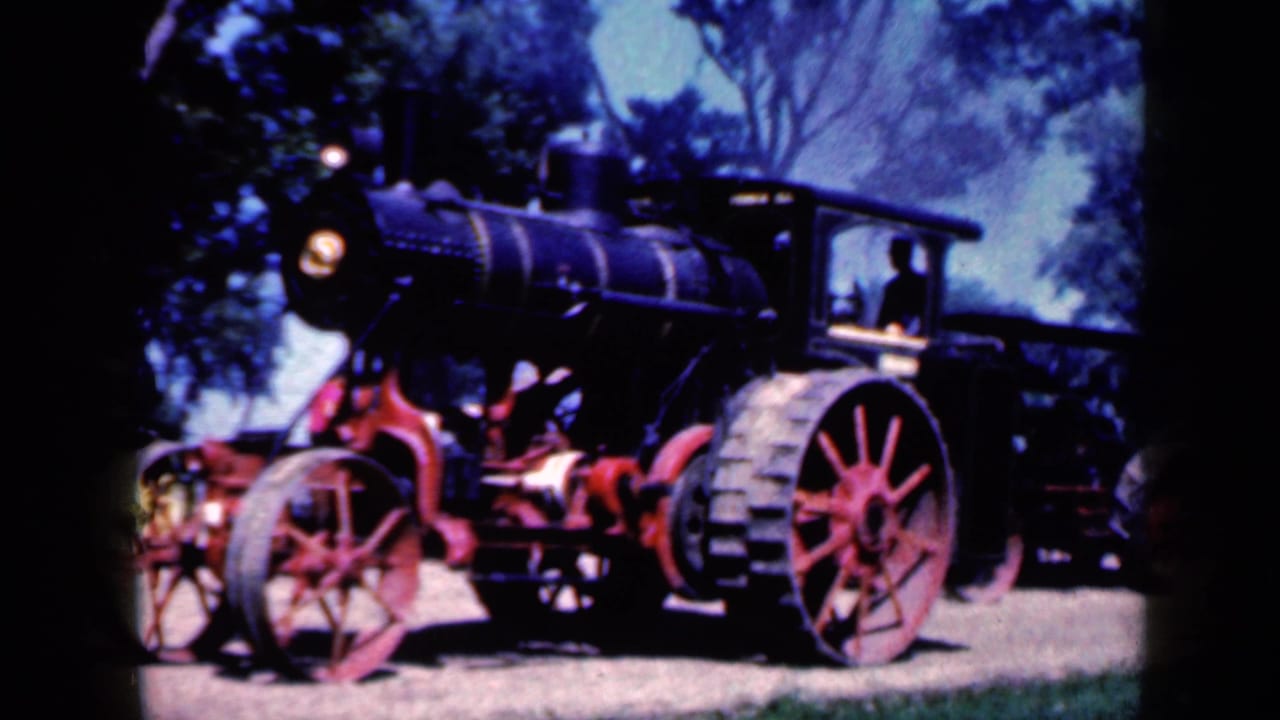Black steam tractor with red wheels and a driver visible in the cab, filmed outdoors in Iowa in 1959.