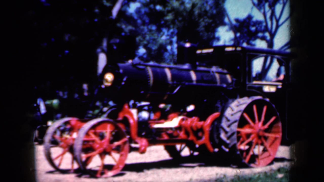 Black steam tractor with red wheels parked under trees.