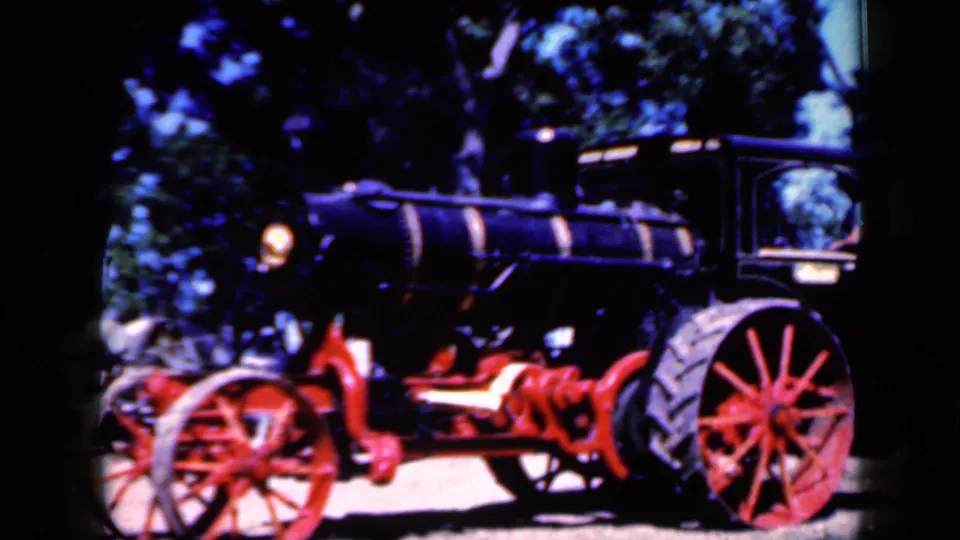 The tractor fills the frame, emphasizing the red spoked wheels, dark boiler, and exposed mechanical parts.