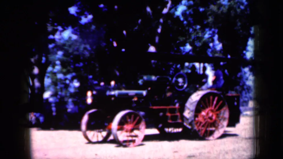 A steam tractor with large red spoked rear wheels and smaller front wheels passes through the frame in 1959 Iowa footage.