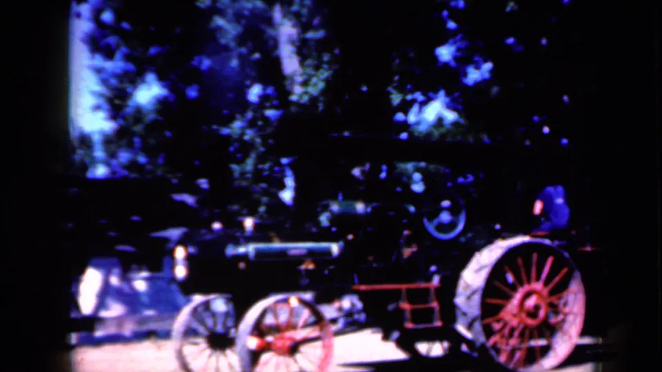 Side view of the steam-powered tractor in 1959 Iowa footage, with red wheels, dark boiler, and a person near the rear operating area.