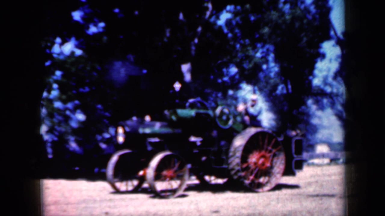 Steam tractor with red-spoked wheels on a dirt path under trees.