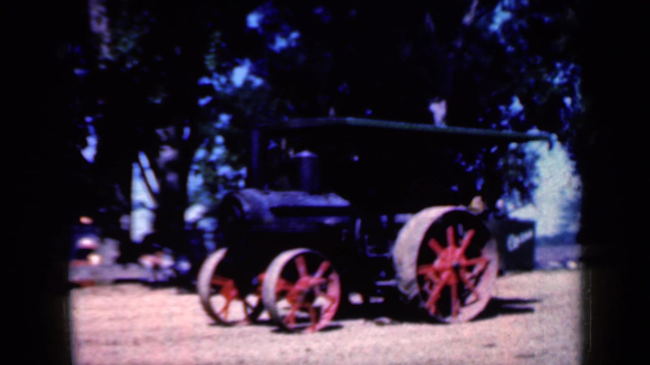 Black steam tractor with red wheels displayed outdoors under trees.