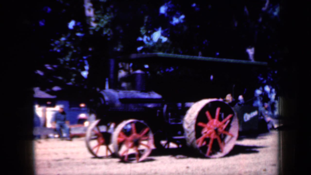 Steam tractor side view with red wheels and people in the background.