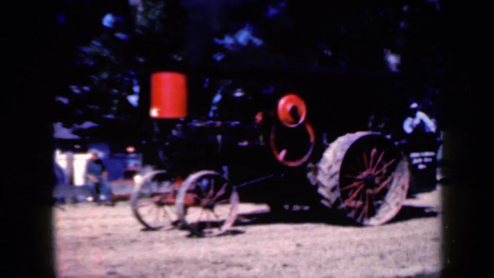 1959 Iowa 8mm frame of the black and red steam tractor from a rear-side angle, with people visible beyond the display.