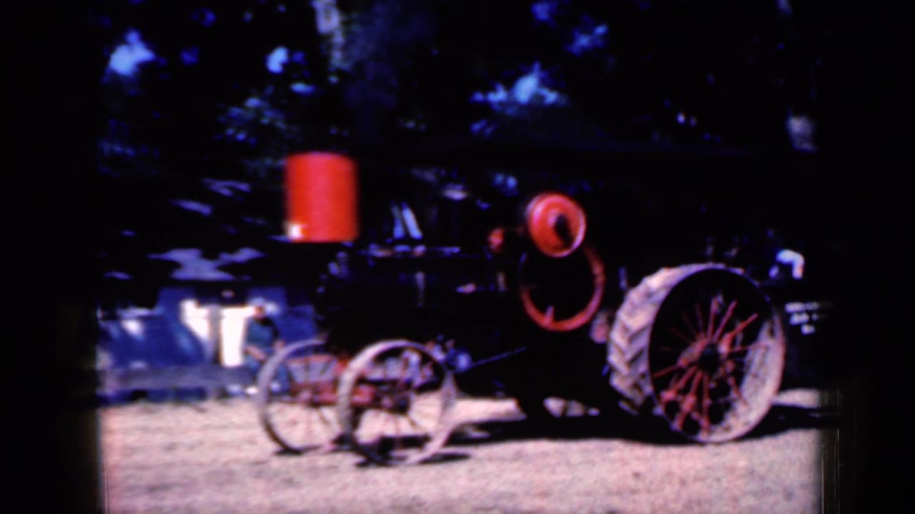 Black vintage tractor with red wheels on dirt under trees.