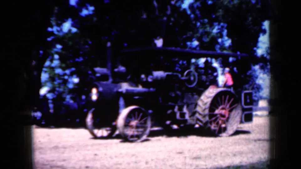 1959 Iowa frame showing a large dark antique tractor with red rear wheel, exposed front wheel structure, and a person in red near the back.