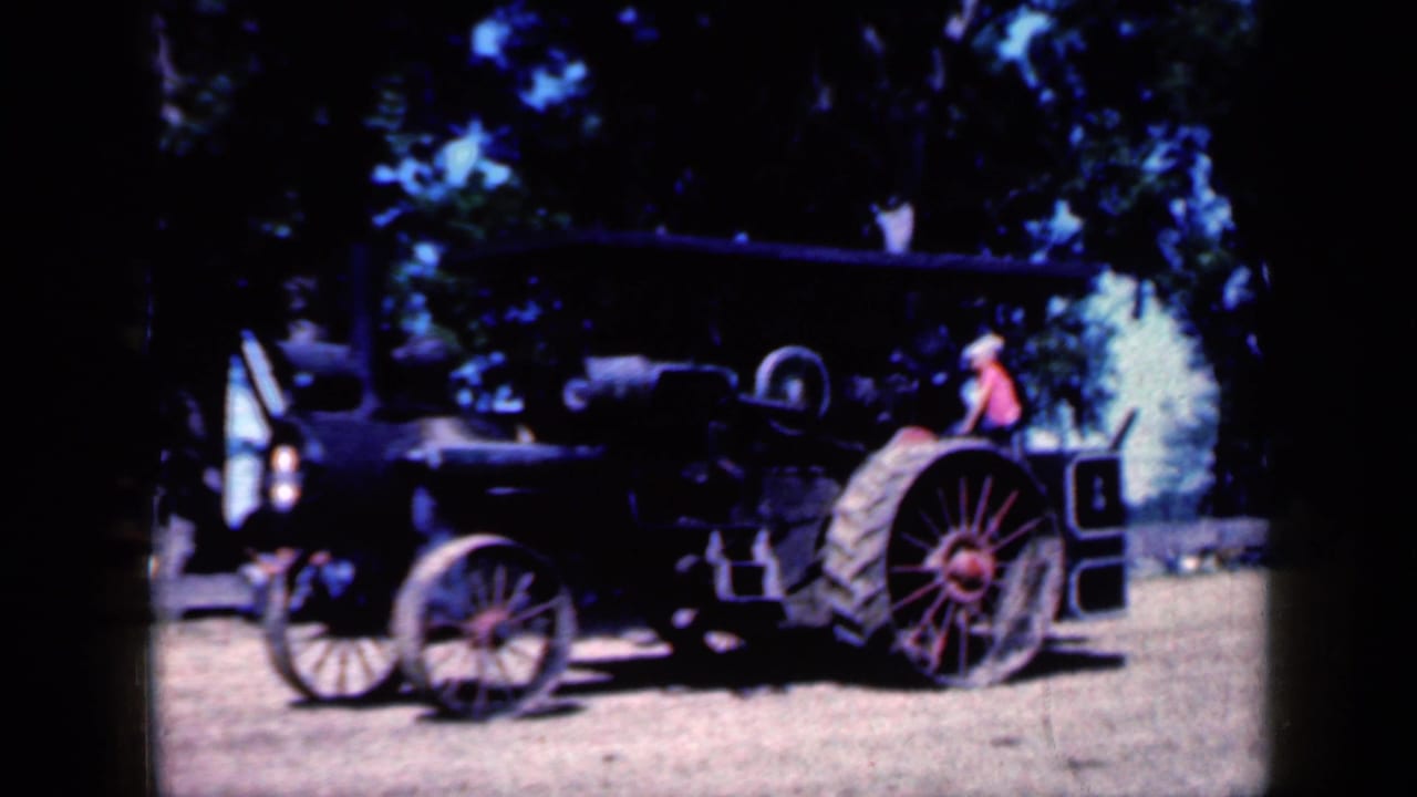 Black steam tractor with large spoked wheels parked on dirt under trees.