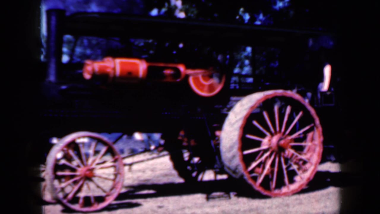 Black and red steam tractor with large spoked wheels on flat ground.