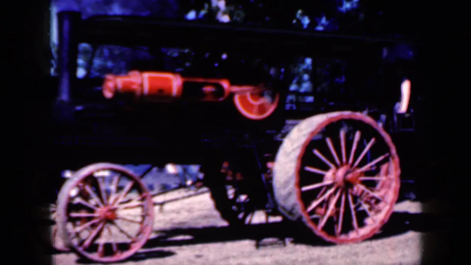 1959 Iowa 8mm frame showing a black and red steam-powered tractor with a boiler and large spoked wheels on flat ground.