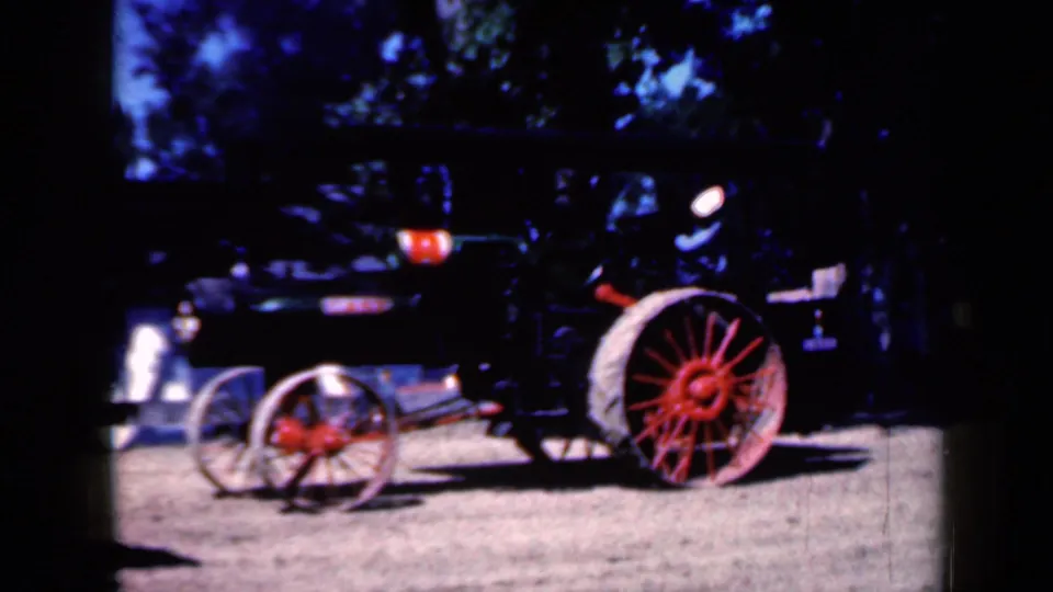 Wider 1959 Iowa 8mm view of the steam tractor on open ground, with large red wheels and indistinct bystanders partly visible.