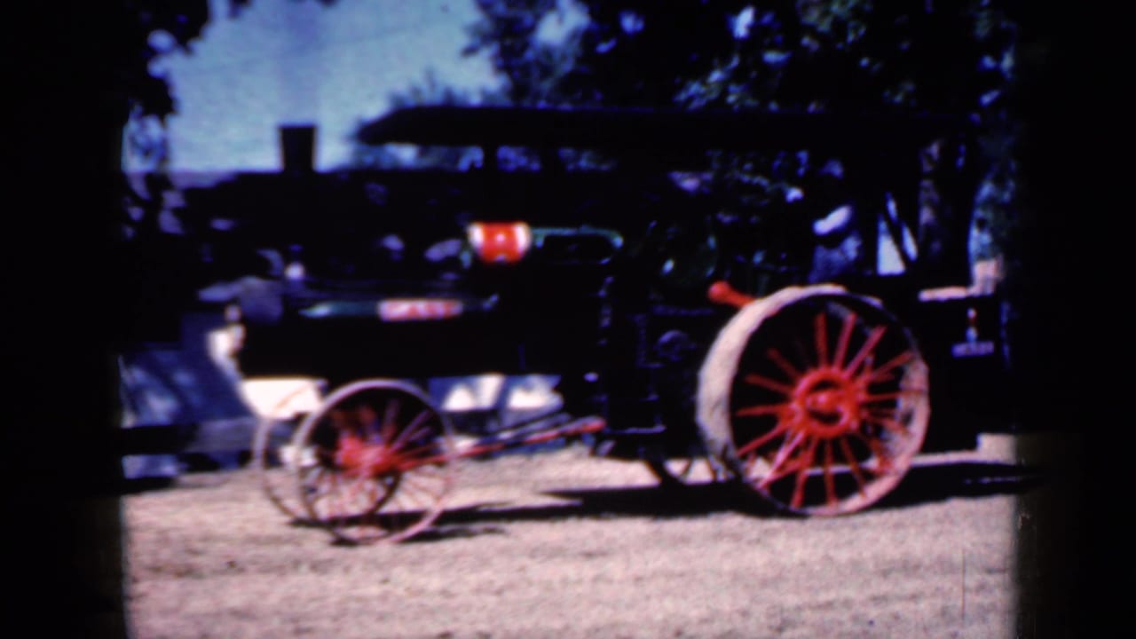 Side view of a steam-powered tractor with red wheels at an Iowa rural fair in 1959 home-movie footage.
