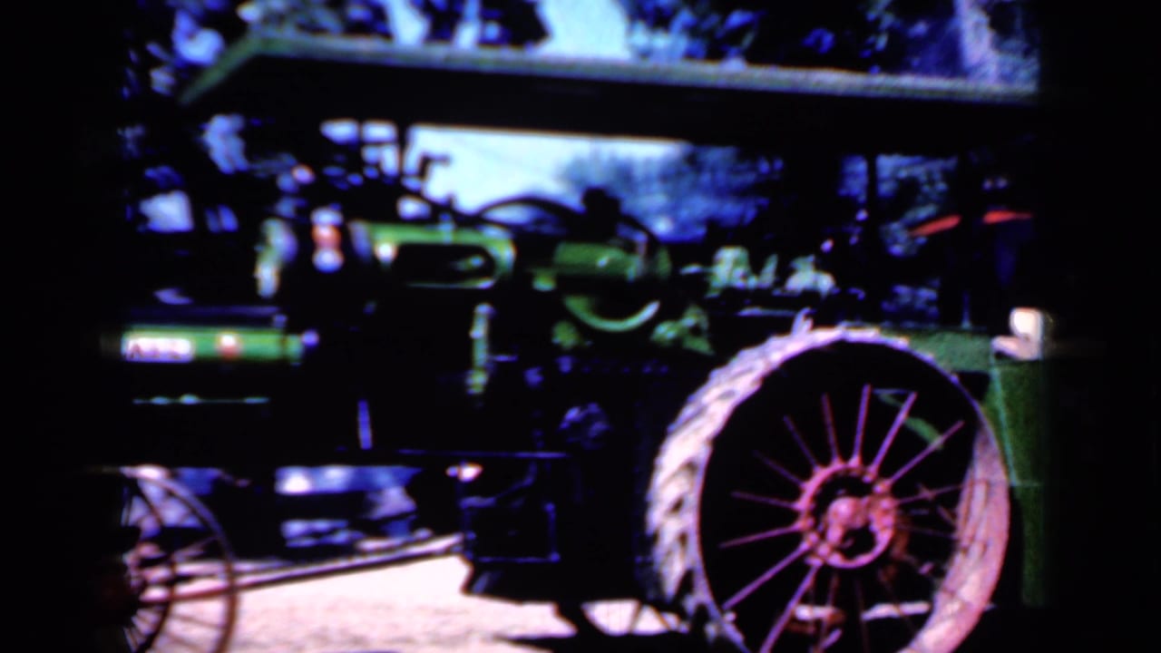 1959 Iowa frame with the tractor closer in view, showing the green boiler body, canopy, smokestack, and large spoked rear wheel.