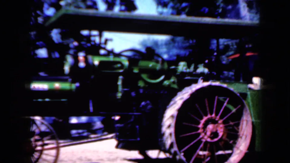 1959 Iowa frame with the tractor closer in view, showing the green boiler body, canopy, smokestack, and large spoked rear wheel.