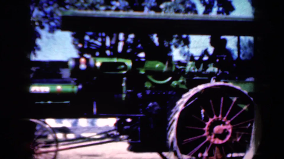 1959 Iowa home-movie frame showing the green steam tractor filling much of the view, with its canopy, smokestack, and red spoked wheel visible.
