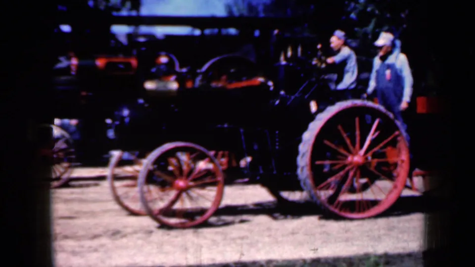 1959 Iowa frame showing two men in caps beside the steam traction engine, with red wheels prominent in the foreground.